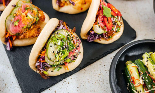 Three steaming hot Bao Bun Rice Classic buns on a bamboo tray